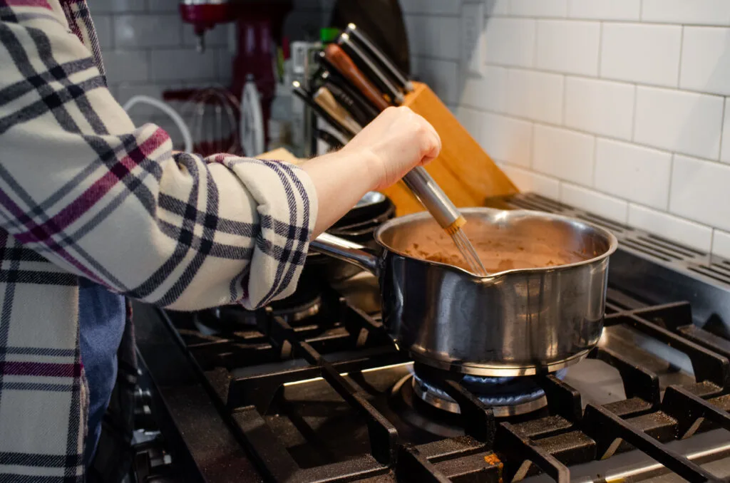 Whisking the pudding on the stove while it cooks to prevent burning and lumps.