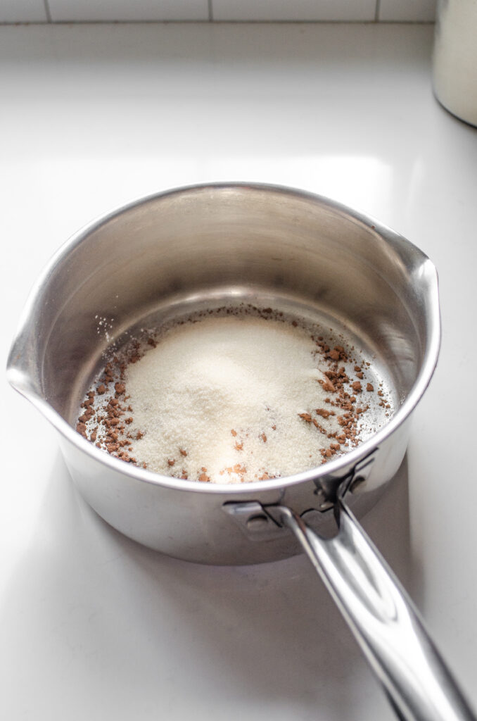 Sugar, cornstarch, salt, and cocoa powder in a medium sized saucepan on a white countertop.