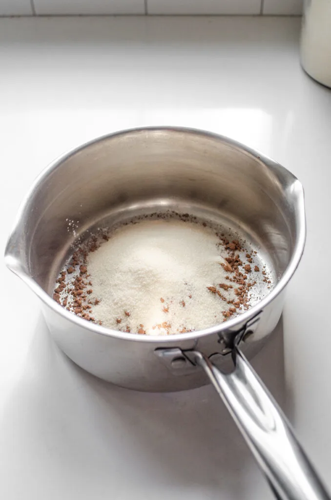 Sugar, cornstarch, salt, and cocoa powder in a medium sized saucepan on a white countertop.