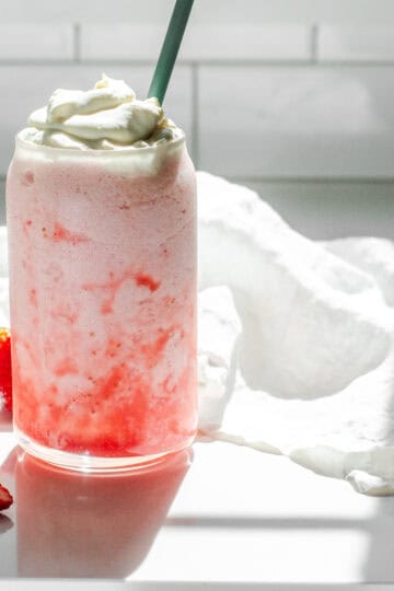 A homemade Starbucks strawberry frappuccino on a white countertop with strawberrys to one side.