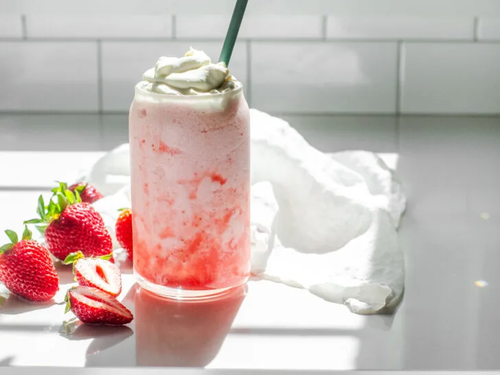 A homemade Starbucks strawberry frappuccino on a white countertop with strawberrys to one side.