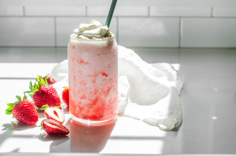 A homemade Starbucks strawberry frappuccino on a white countertop with strawberrys to one side.
