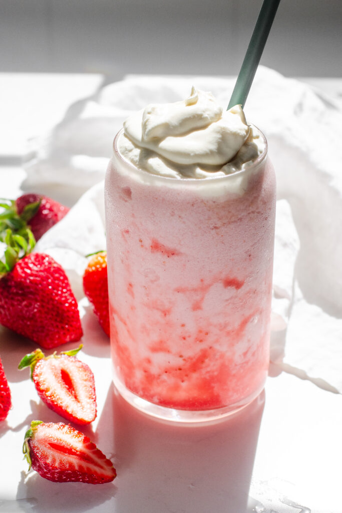 A homemade strawberry frappuccino on a white countertop with fresh strawberries on one side, and a linen napkin on the other.
