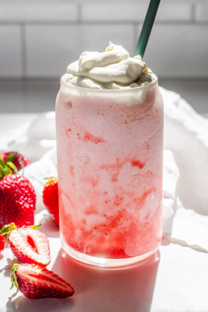 A homemade strawberry frappuccino on a white countertop with fresh strawberries on one side, and a linen napkin on the other.