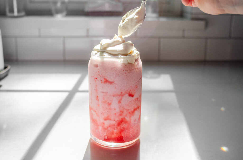 Adding the whipped cream on top of the frappuccino in the glass.