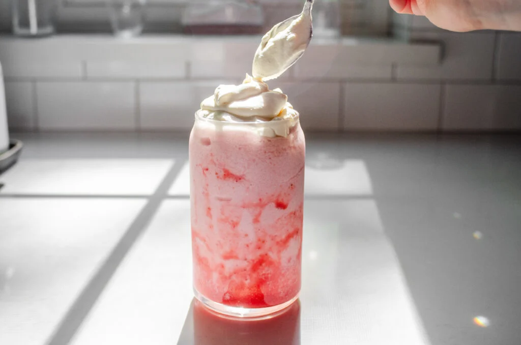 Adding the whipped cream on top of the frappuccino in the glass.