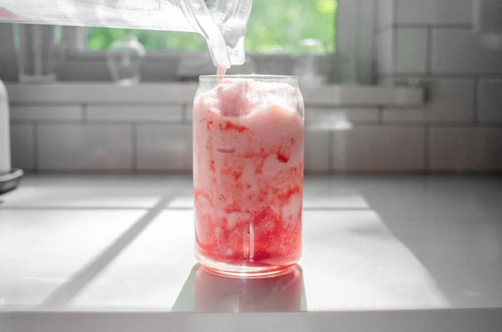Pouring the strawberry frappuccino into the prepared glass.