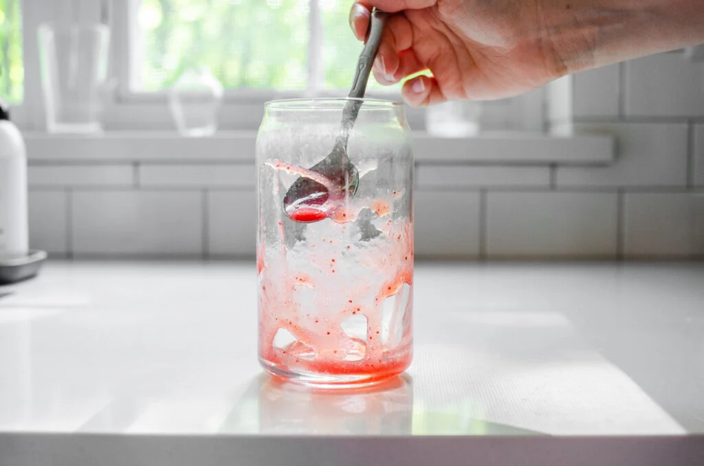 Drizzling strawberry puree into a glass.