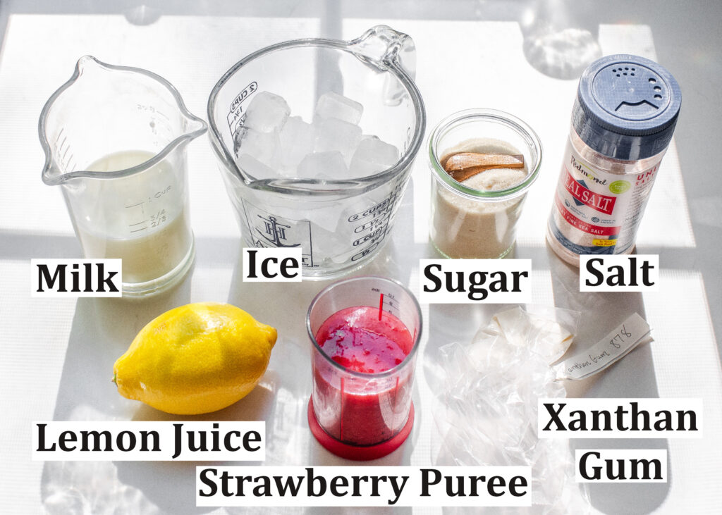All of the ingredients needed to make a strawberry frappuccino laid out on a white countertop.