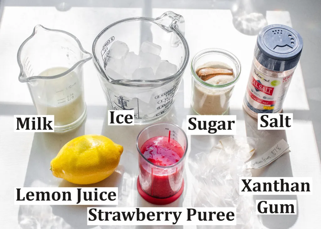 All of the ingredients needed to make a strawberry frappuccino laid out on a white countertop.
