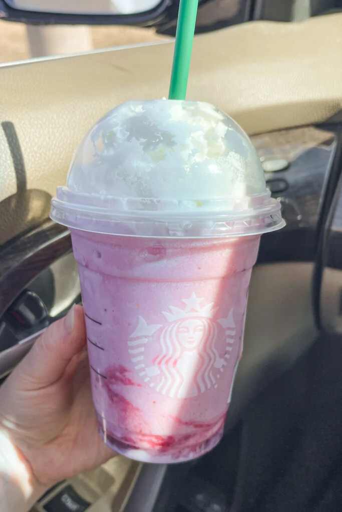 Holding a Starbucks strawberry creme frappuccino.