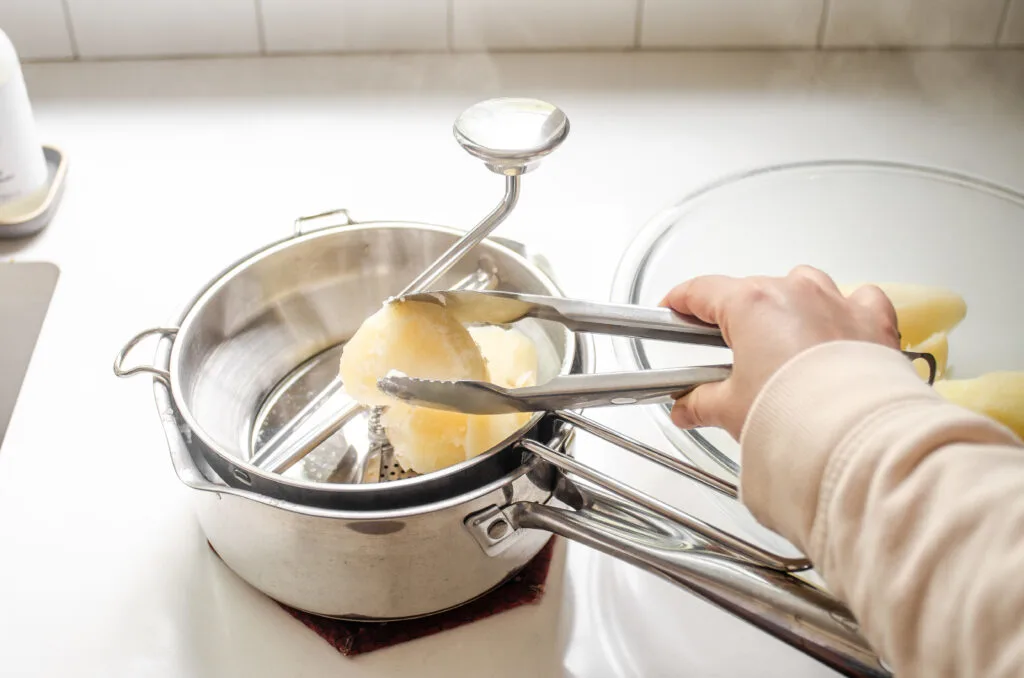 Adding potatoes to a food mill with tongs.