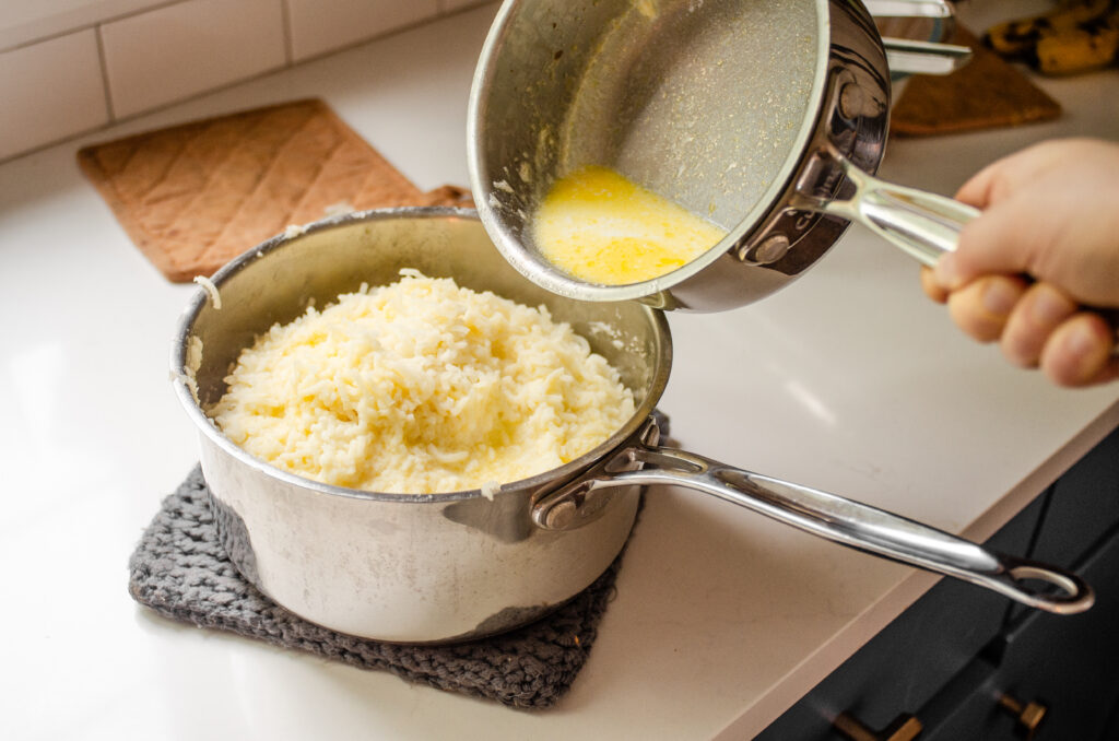 Pouring the mleted butter and warmed milk over the riced potatoes.