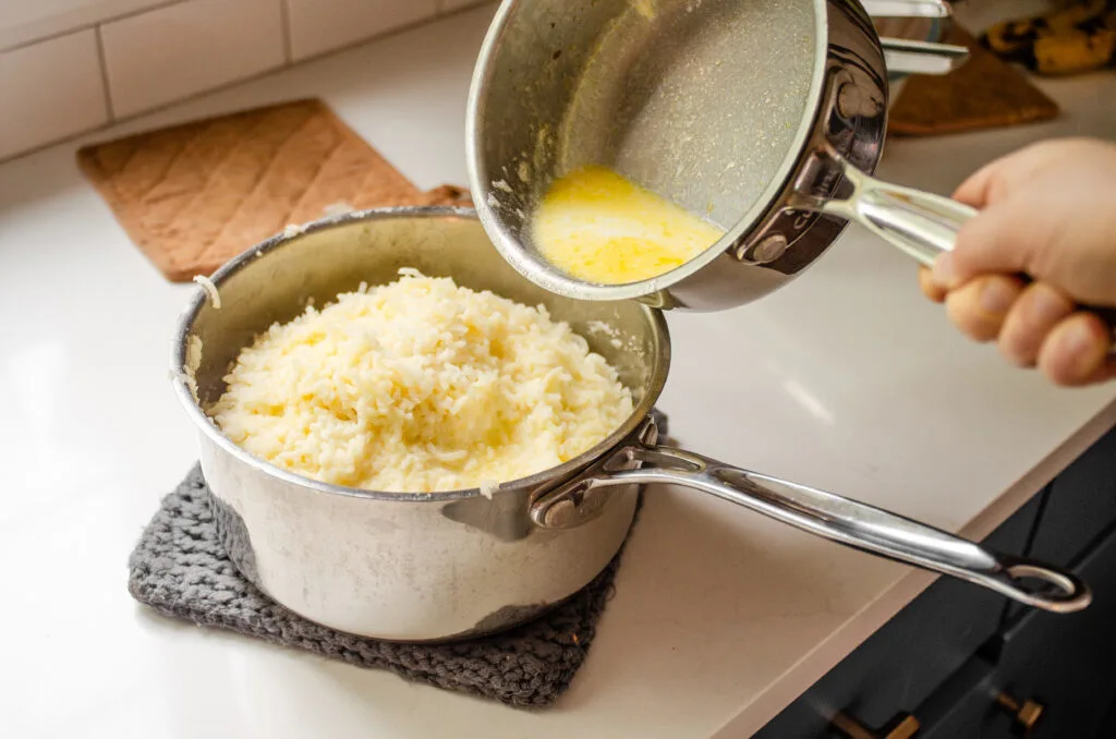 Pouring the mleted butter and warmed milk over the riced potatoes.
