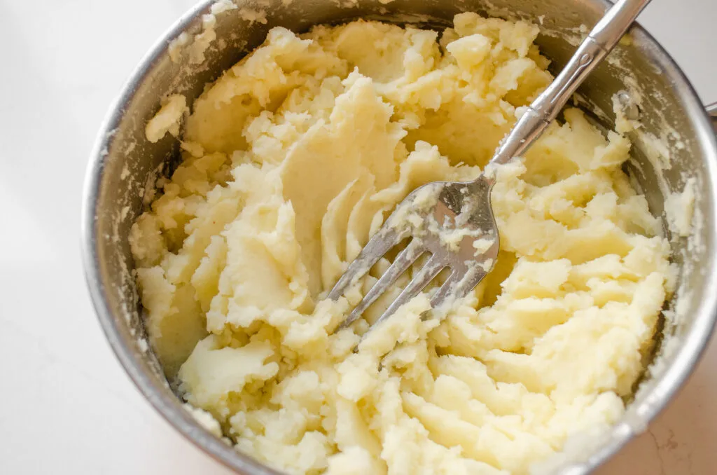 A close up photo of potatoes mashed with a fork.