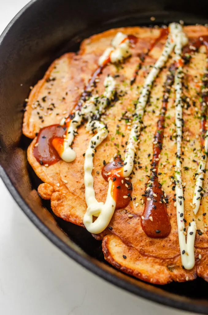 A close up shot of the sourdough discard kimchi pancake in the skillet with mayonnaise, sriracha, and sesame seeds on top.