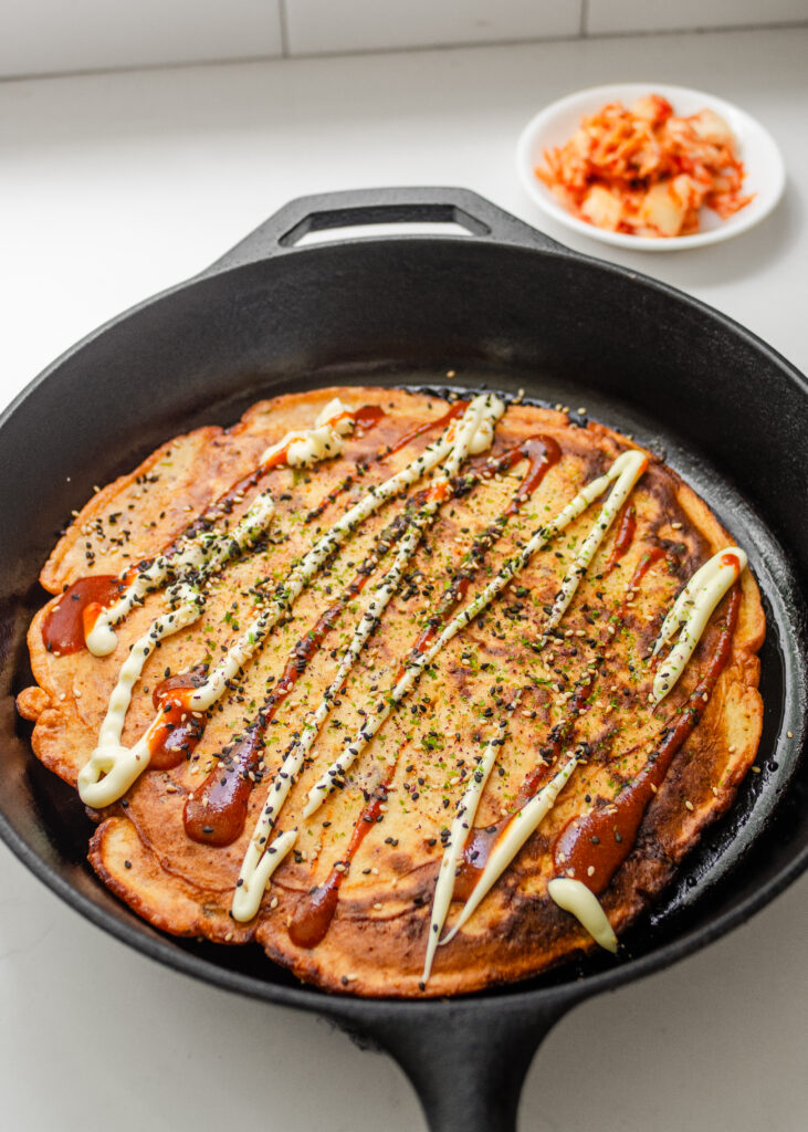 The pancake with the optional toppings and a bowl of kimchi in the background. 