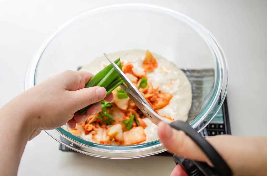 Cutting green onions on top of the kimchi and sourdough starter in the bowl.