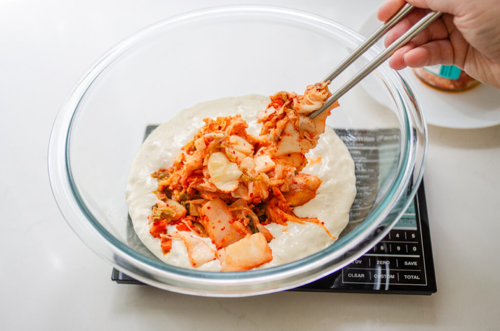 Adding kimchi to the sourdough discard with chopsticks. 