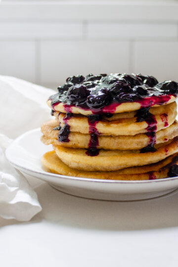 A stack of pancakes on a plate with fresh blueberry compote on top.