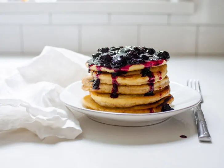 A stack of pancakes on a plate with fresh blueberry compote on top.