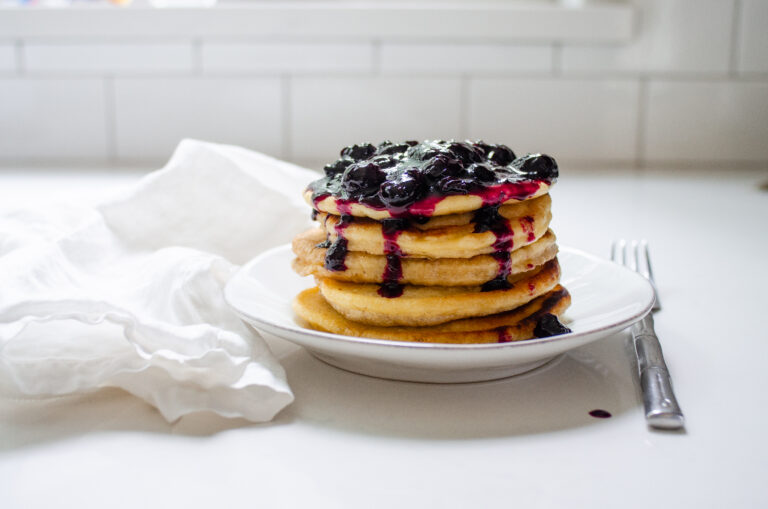 A stack of pancakes on a plate with fresh blueberry compote on top.