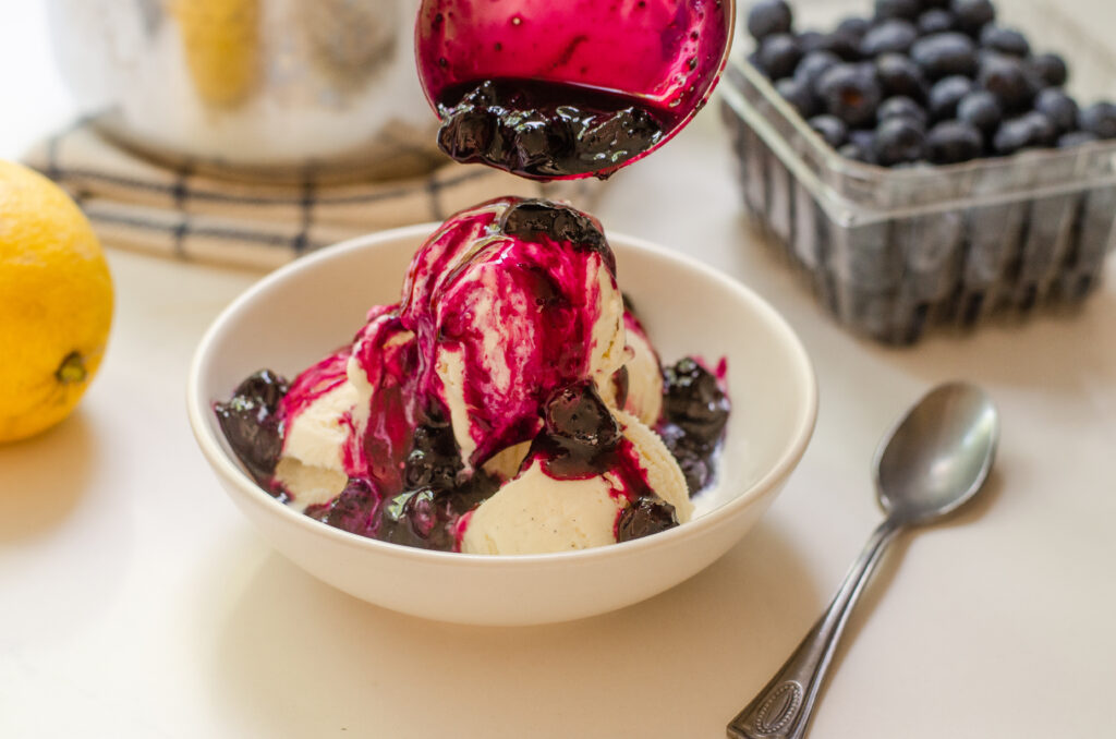 Pouring warm blueberry compote over vanilla ice cream.