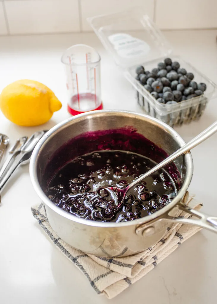 A saucepan of blueberry compote with a fresh lemon and fresh blueberries behind it.