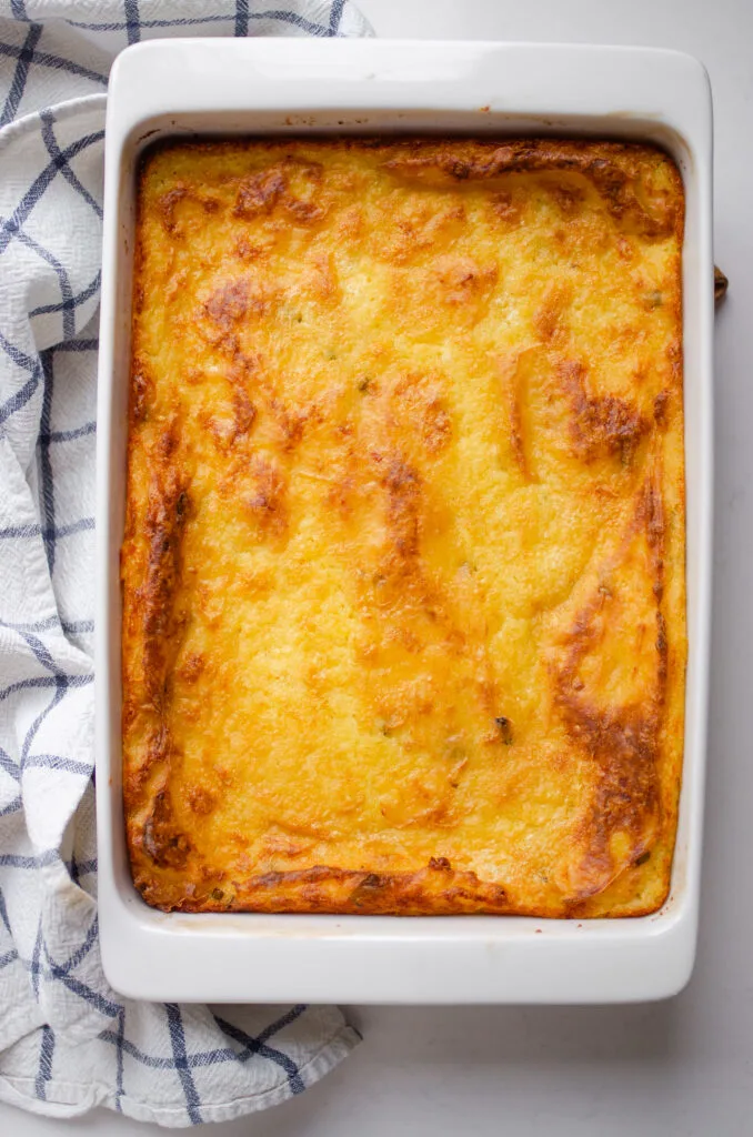 The finished baked mashed potatoes in the baking dish with a tea towel off to the side.