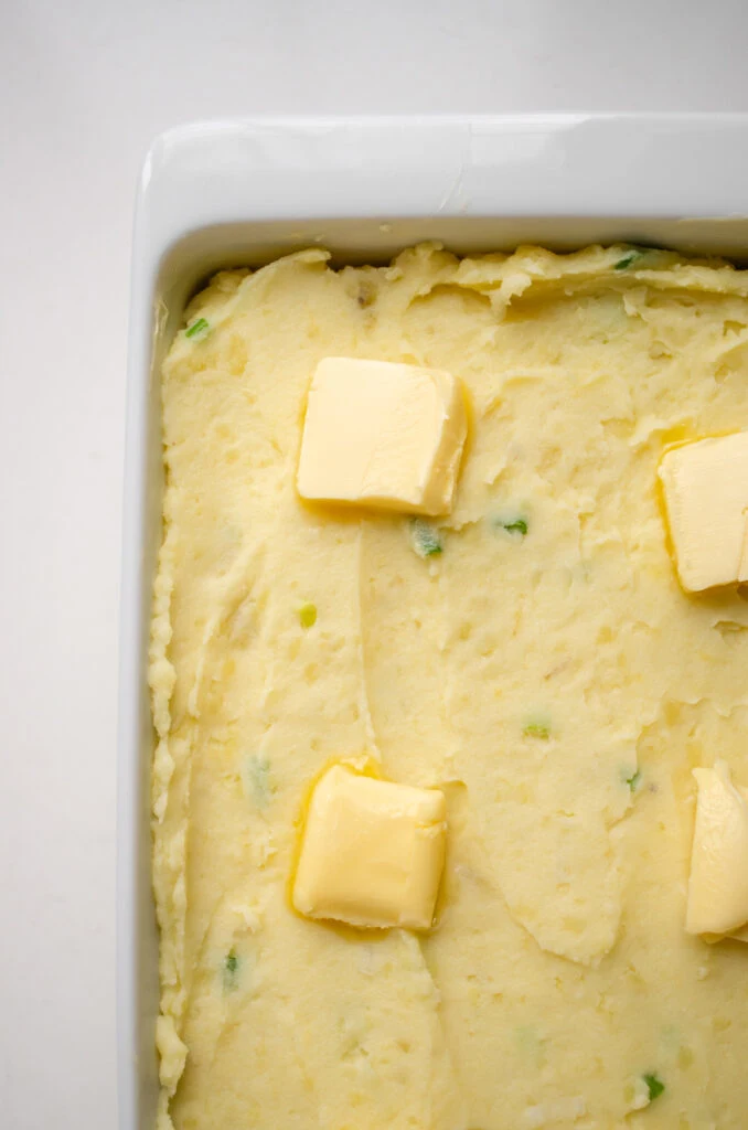 The mashed potatoes in the baking dish with pats of butter on top.