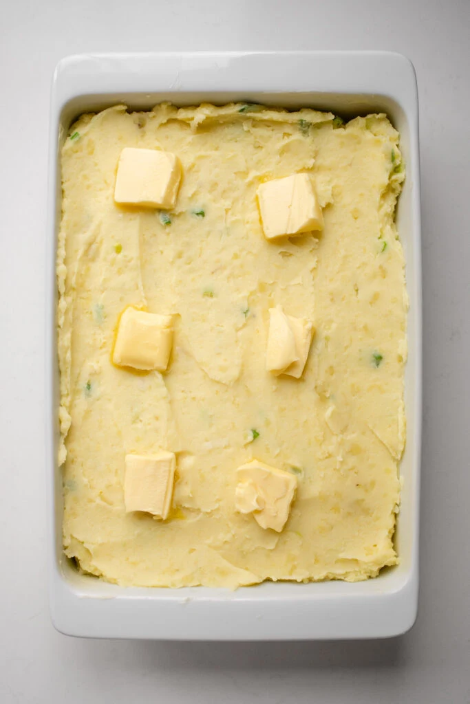 The mashed potatoes in the baking dish with pats of butter on top.