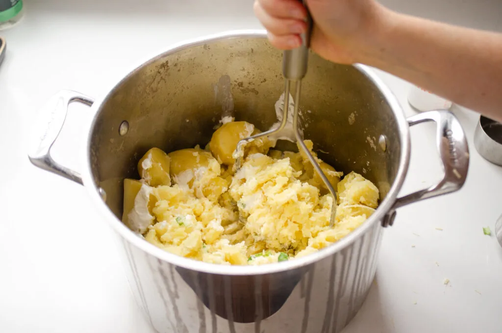 Mashing the potatoes along with the other ingredients in the pot.