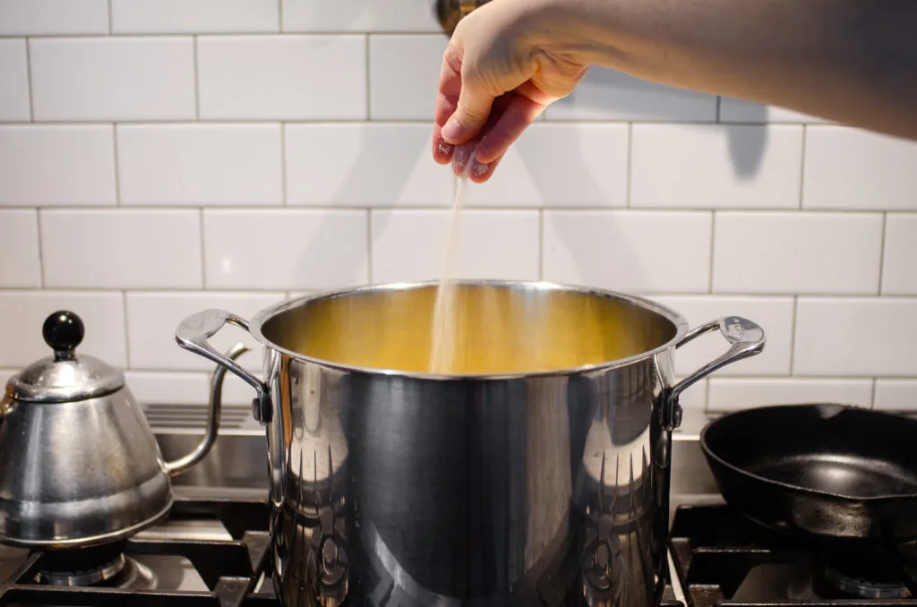 Adding salt to the pot of potatoes.