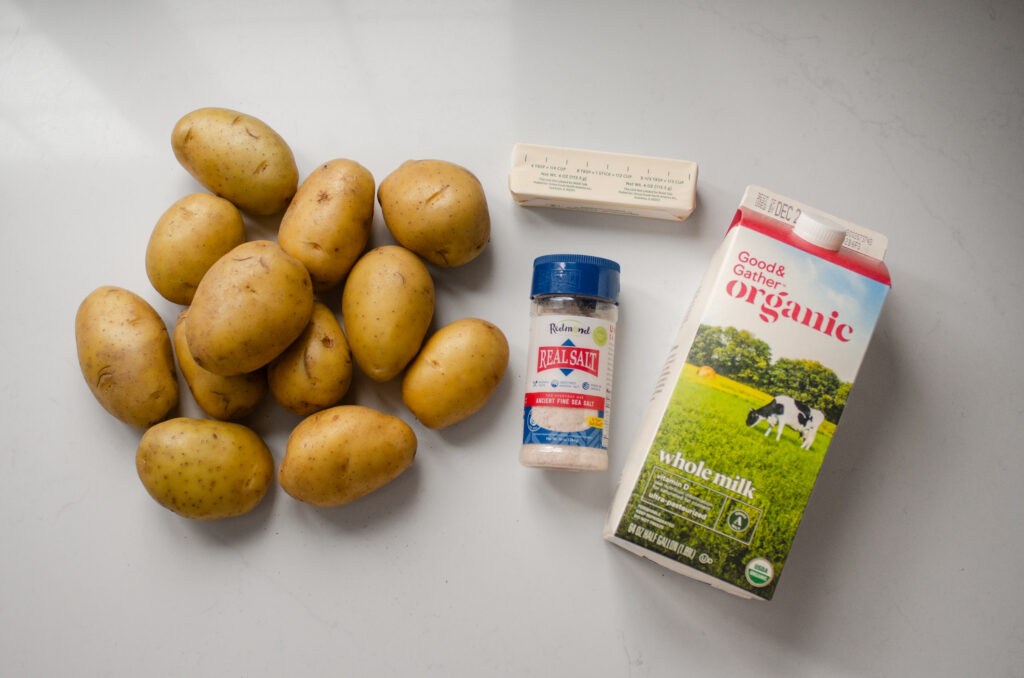 All of the ingredients needed to make simple baked mashed potatoes laid out on a white countertop.