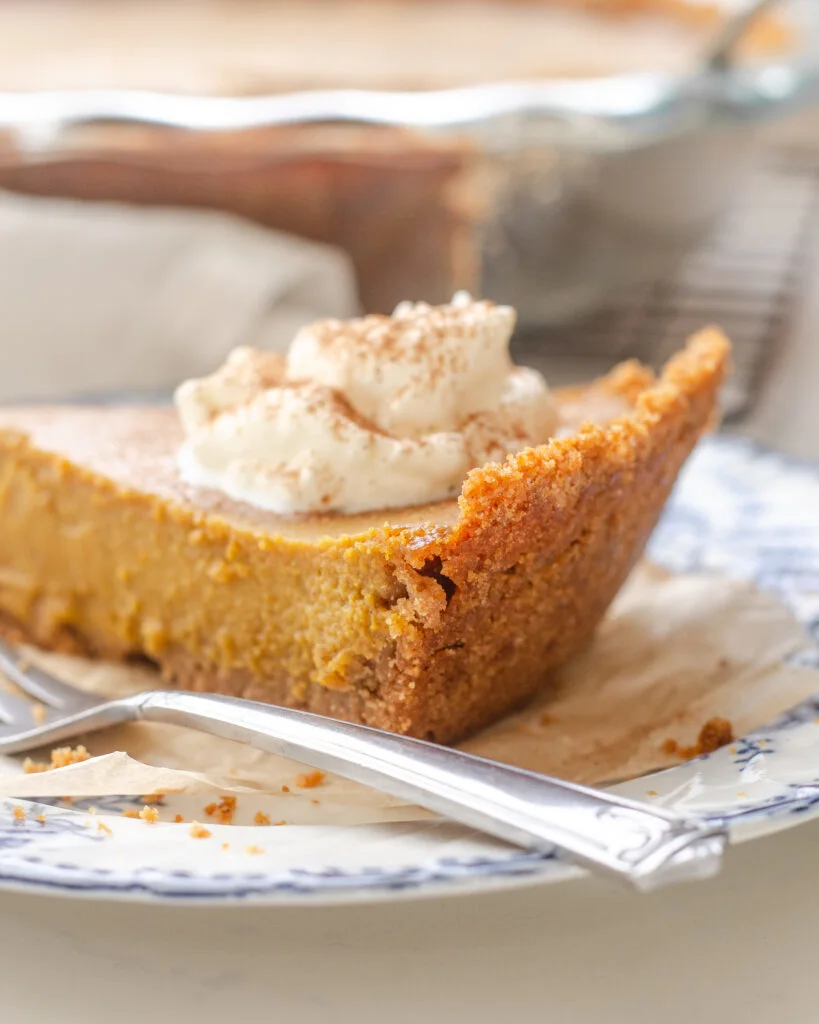 A side view of a slice of pumpkin pie to showcase the graham cracker crust.