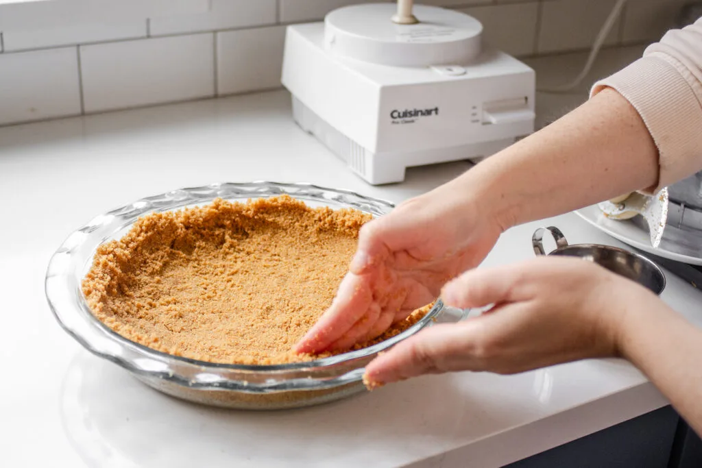 Pressing the graham cracker crust into the pan.