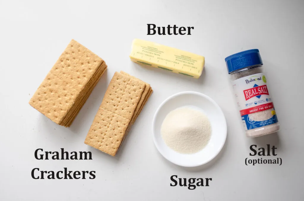 All of the ingredients needed to make a graham cracker crust laid out on a white countertop. 