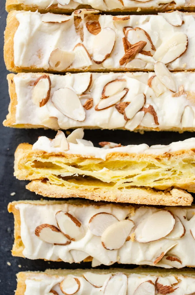 Slices of Danish puff pastry on a black slate board with one slice turned on its side so you can see the layers.