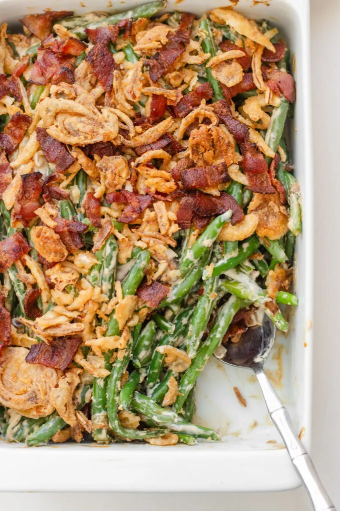 A pan of green bean casserole with bacon and fried onions with a scoop taken out.