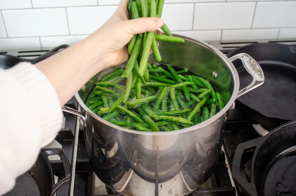 Putting fresh green beans into a pot of boiling water.