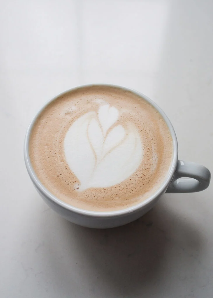 A vanilla latte with latte art on a white countertop.