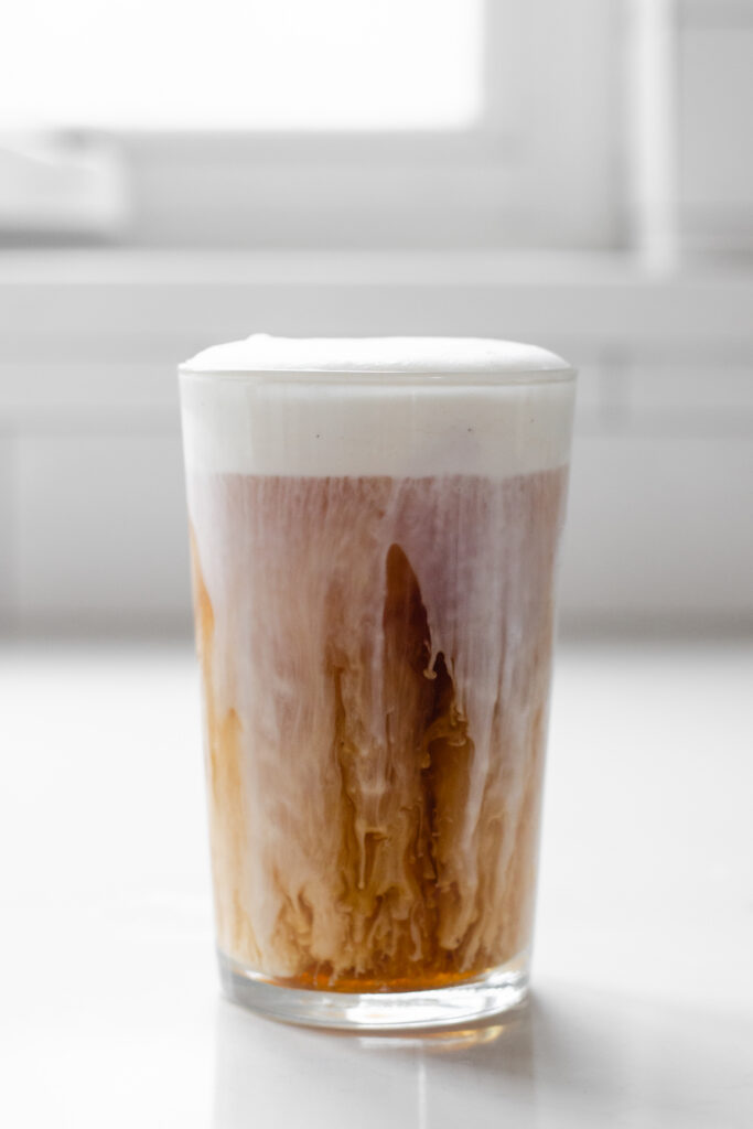 An iced London Fog latte in a glass with cold foam slowly melding into the drink.
