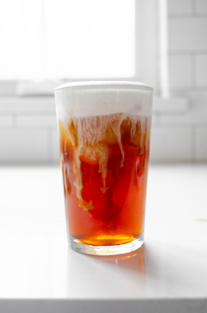 An iced London Fog latte in a glass with cold foam slowly melding into the drink. 