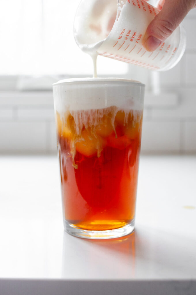 Pouring the sweet cream on top of the brewed tea in the glass.
