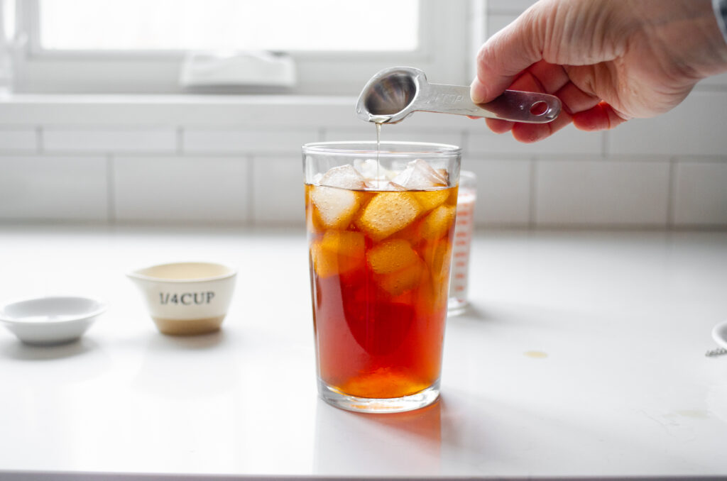 Adding the vanilla syrup to the iced tea in the glass.