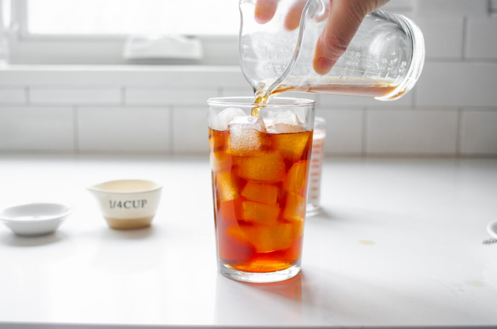 Pouring the brewed tea over the ice in the glass.
