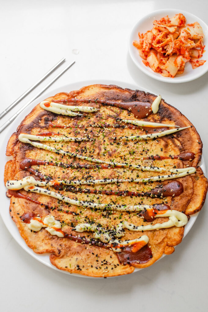 A sourdough discard kimchi pancake on a dinner plate with a bowl of kimchi in the background.