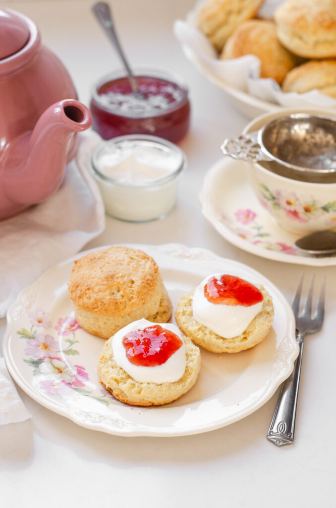 Two sourdough scones on a fancy plate with a pink teapot and a floral teacup in the background.