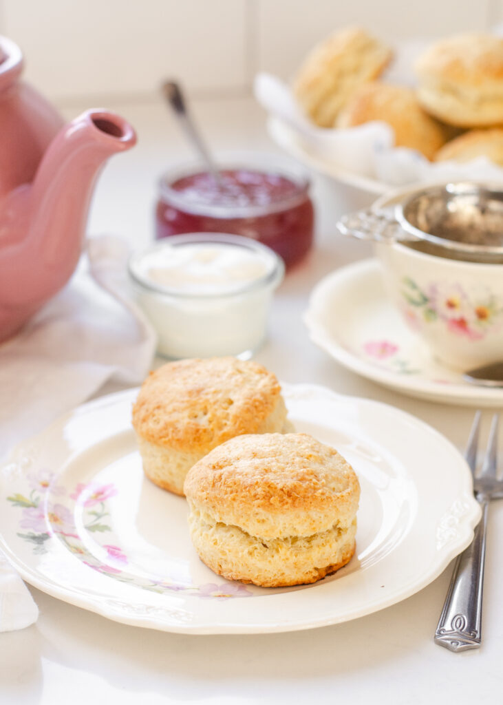 Two sourdough scones on a fancy plate with a pink teapot and a floral teacup in the background.
