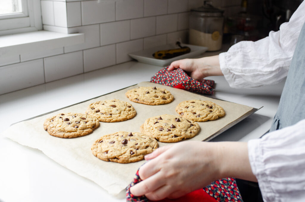 Placing a baking sheet of baked einkorn chocolate chip cookies onto a counter to cool for 5 minutes.